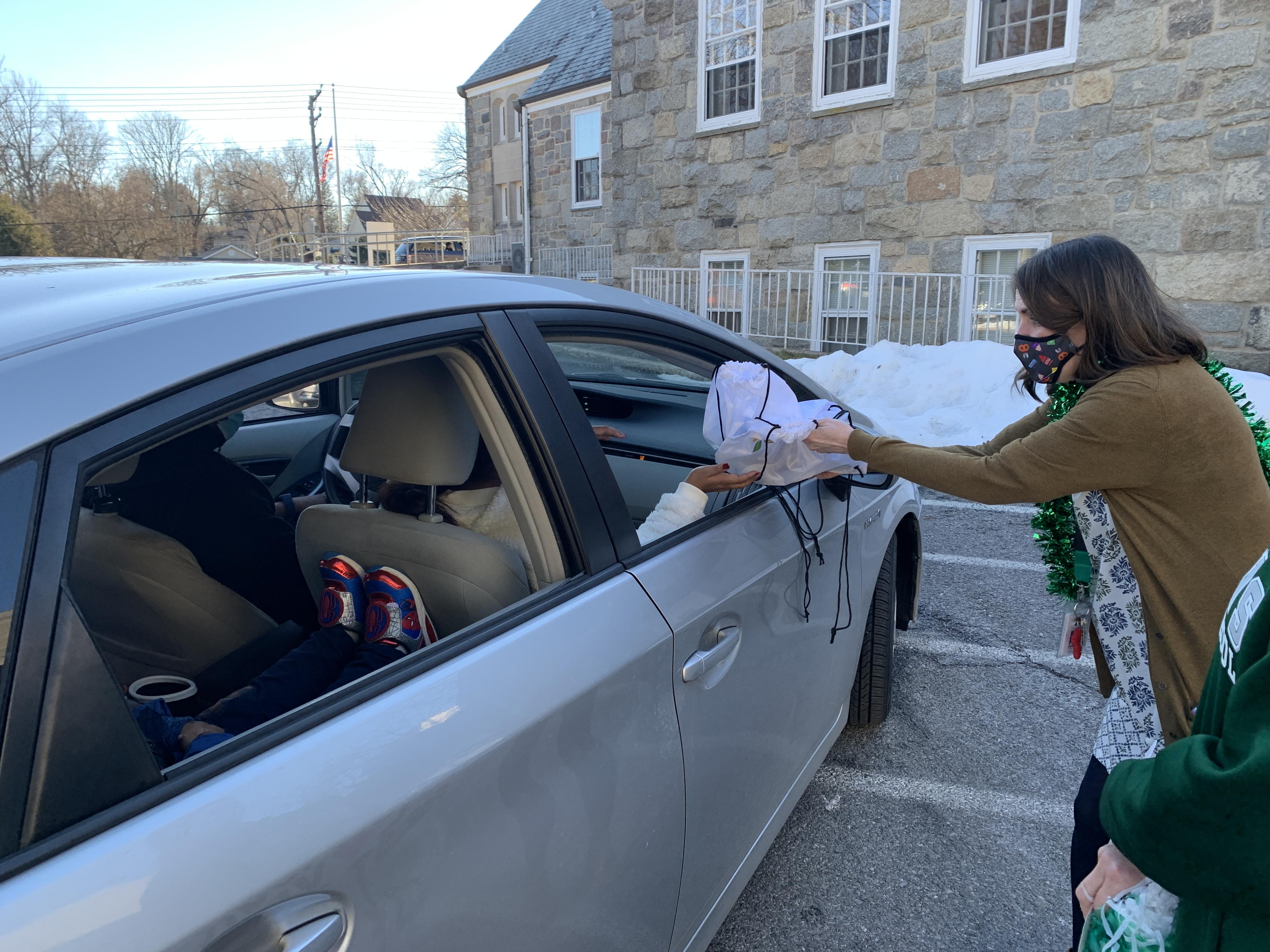 teacher giving parent swag bag through car window