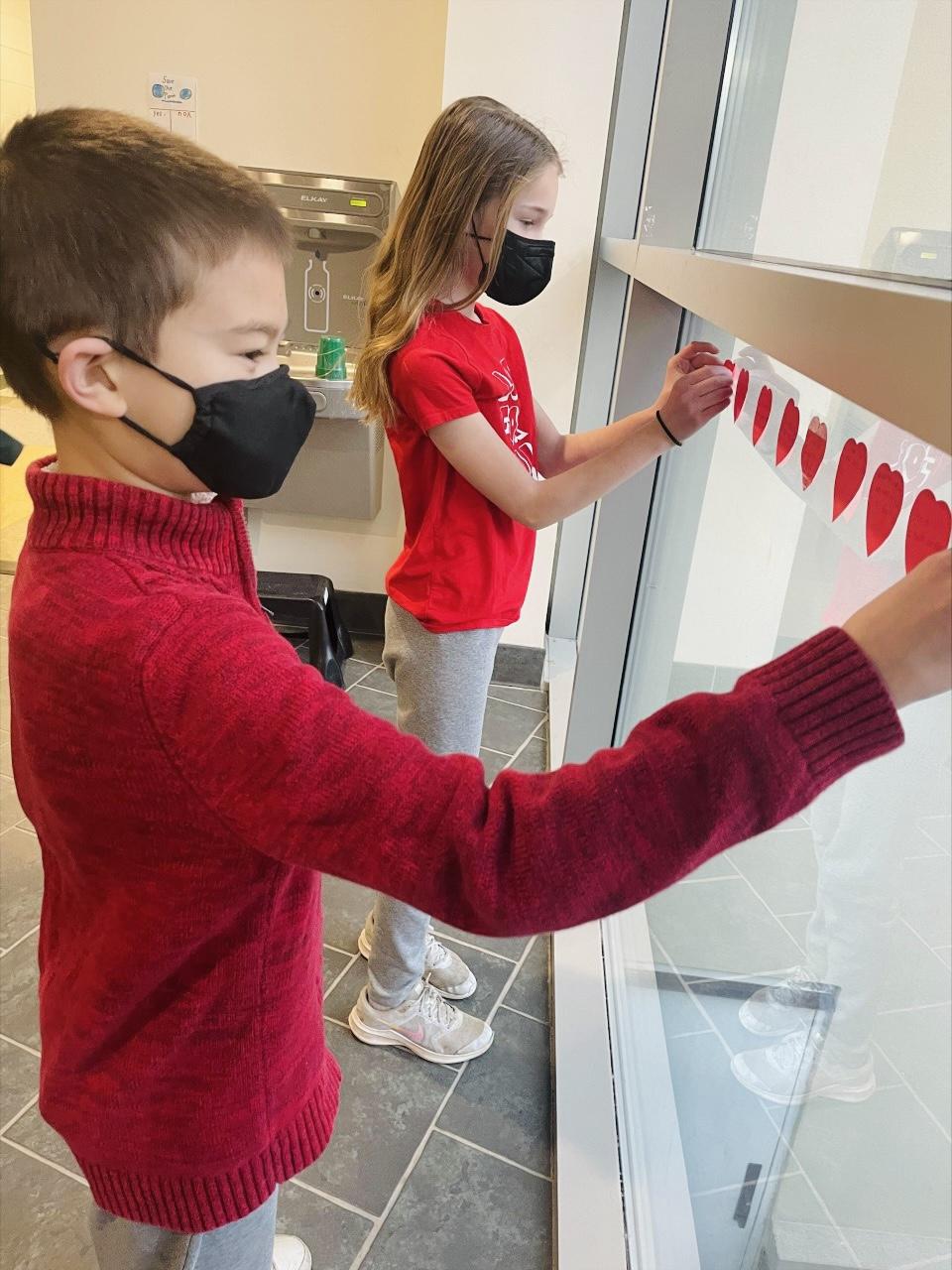 students putting up heart shaped kindness notes on the school walls