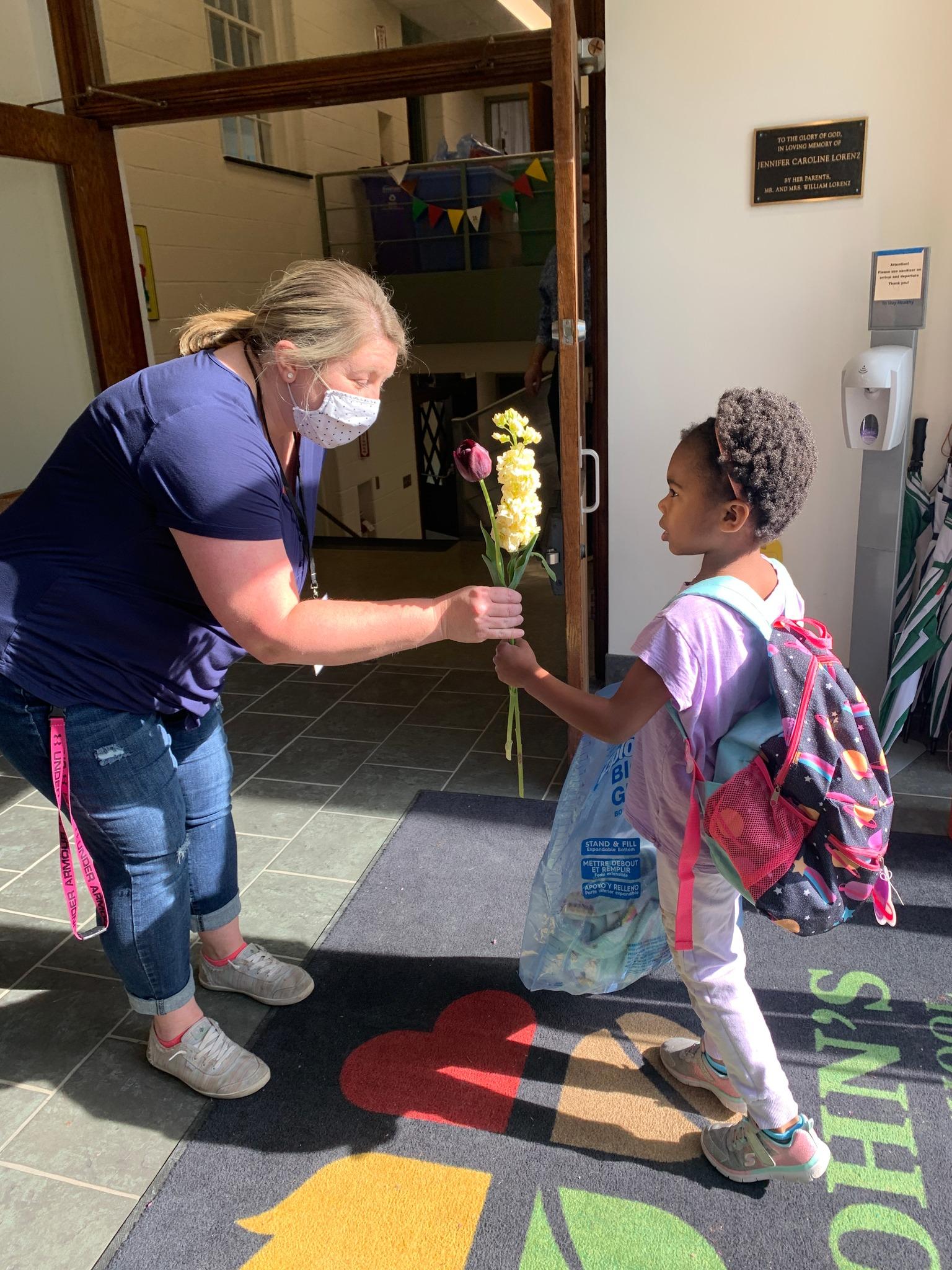 Parent volunteer handing out flowers to students 